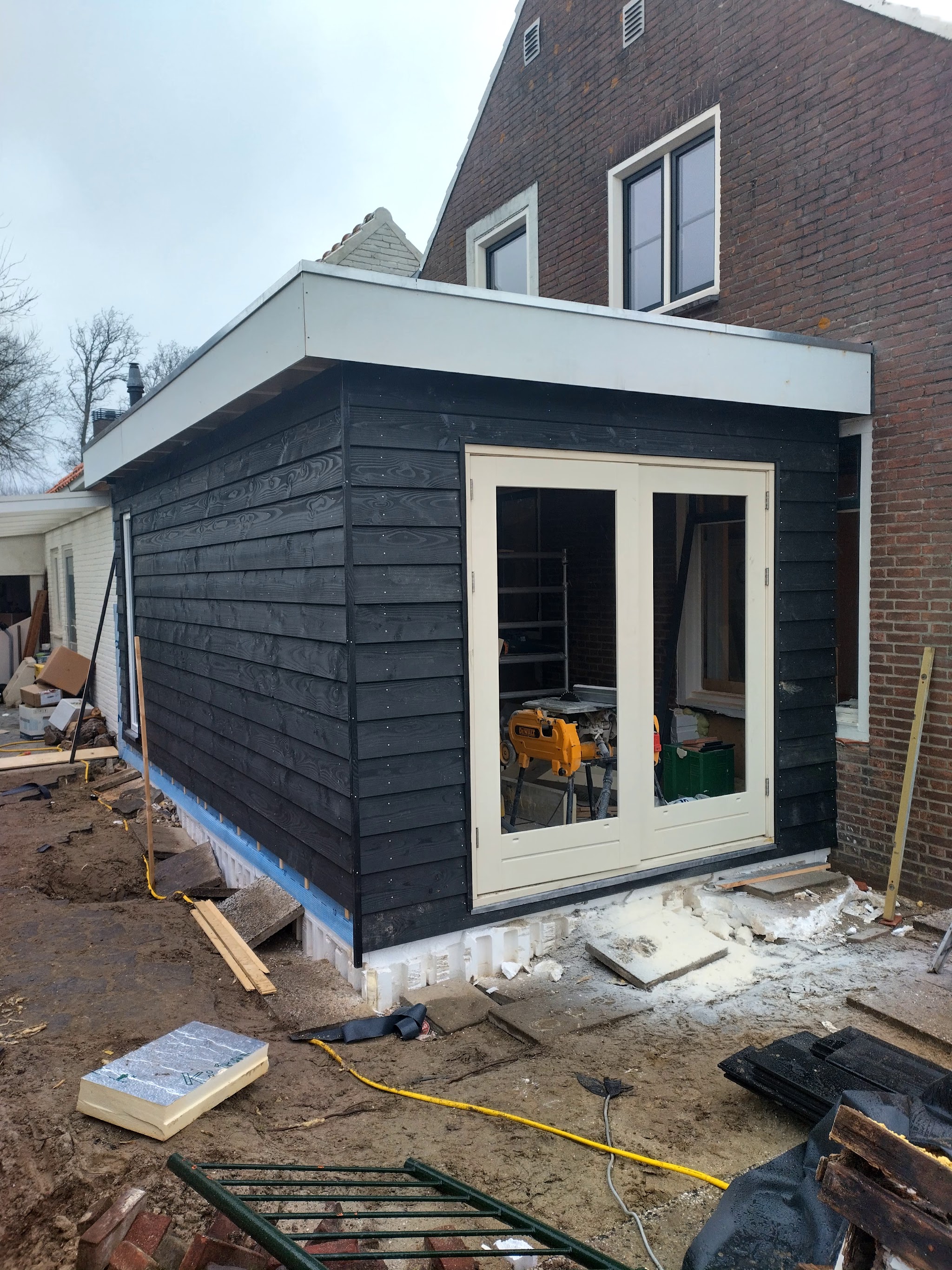 Nieuwe aanbouw met zwarte houten gevelbekleding en dubbele tuindeuren, in aanbouw