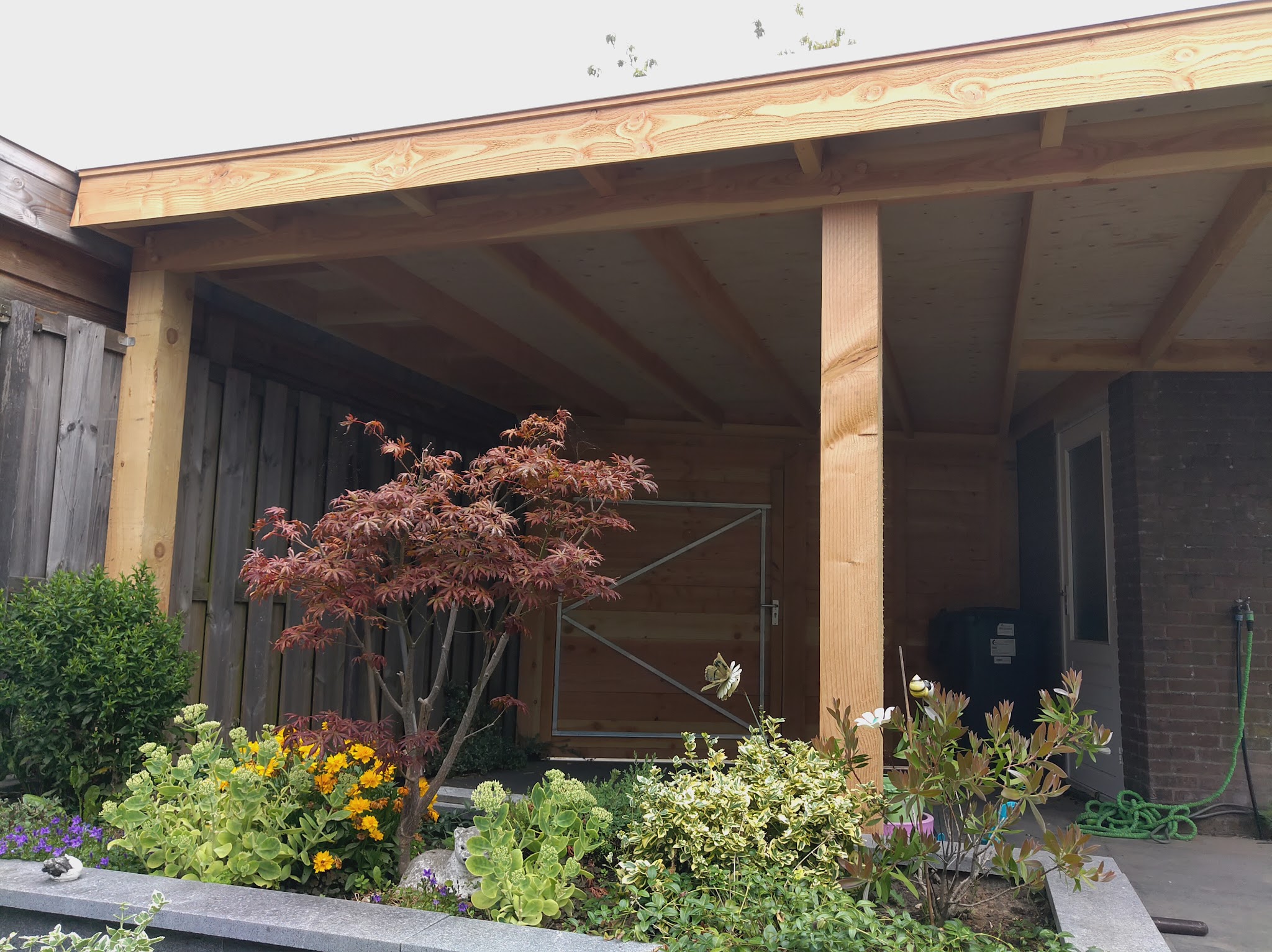 Afgewerkte houten veranda in een tuin met beplanting ervoor